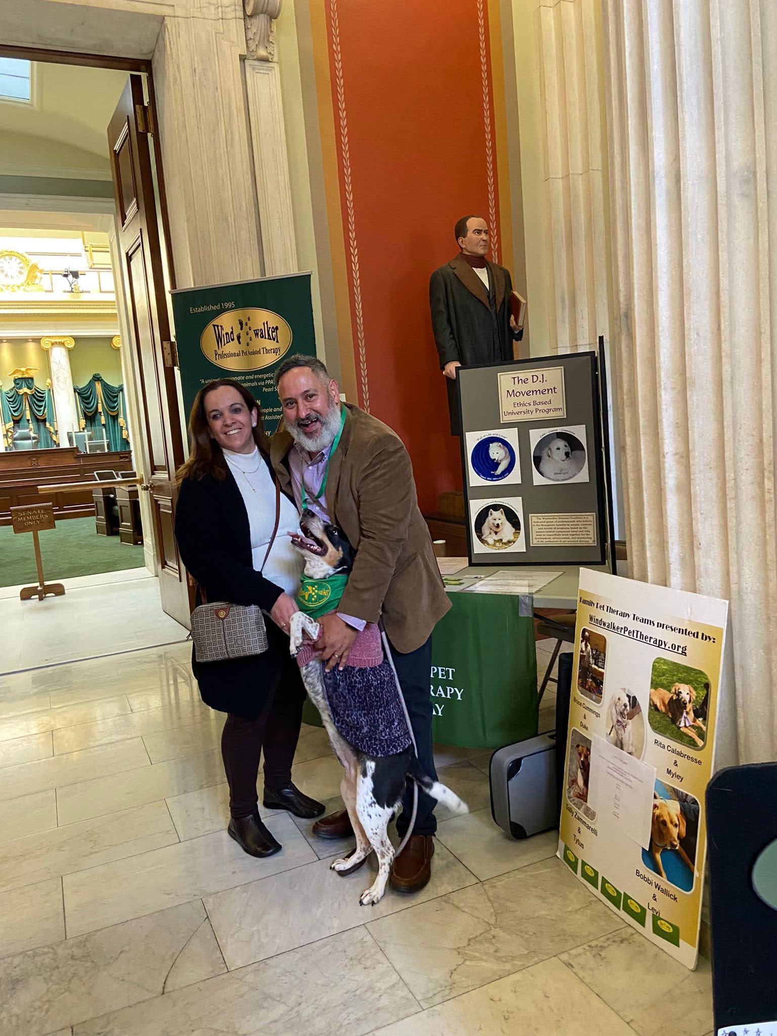 Carlos Moriella and July DeSousa with Mia beside pet-assisted activity information