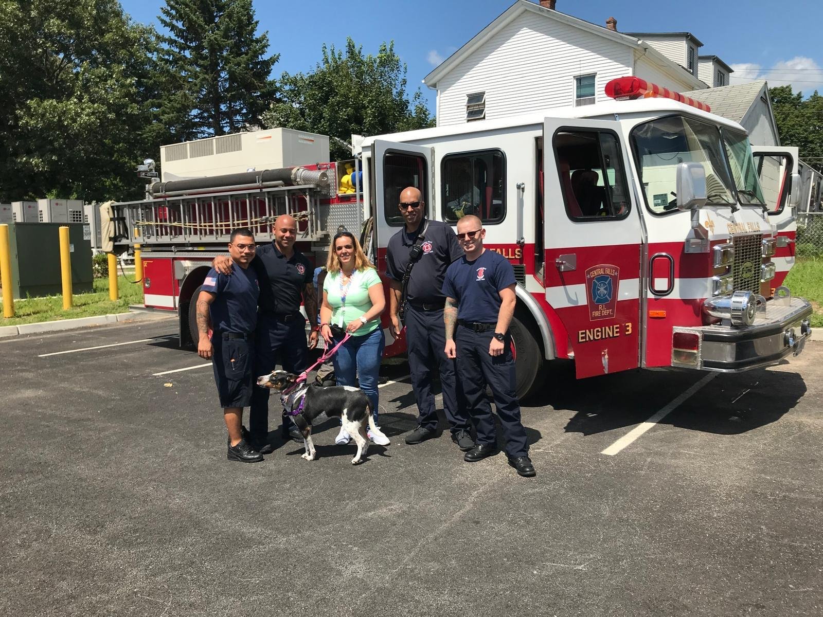 A handler and dog with local emergency personnel beside a fire vehicle at a community event